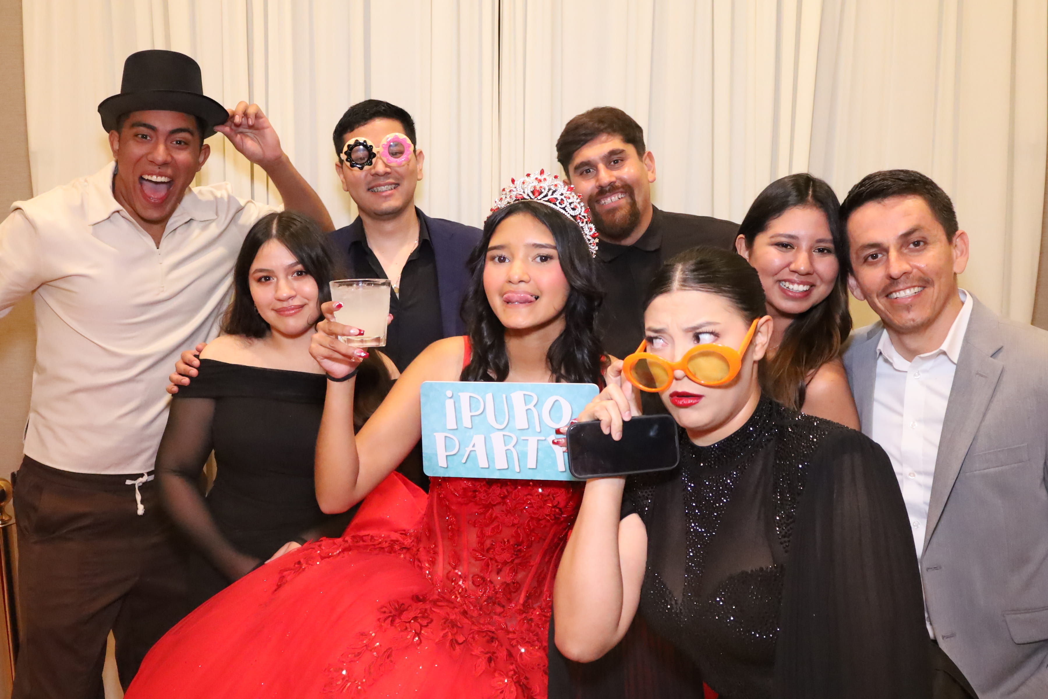Quinceañera with family holding a '¡PURO PARTY!' sign on a beige drape
